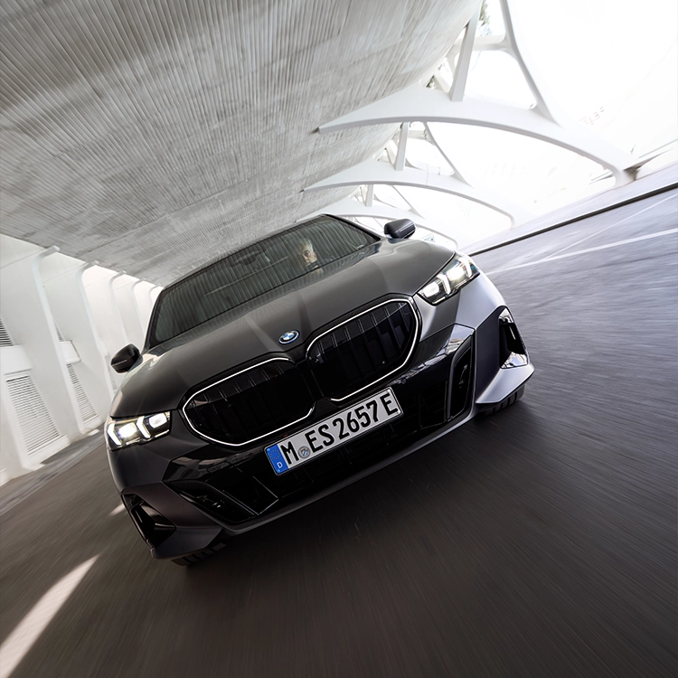 Der neue BMW 5er fährt elegant eine breite Allee entlang, verkörpert Luxus, Innovation und sportliche Fahrdynamik.